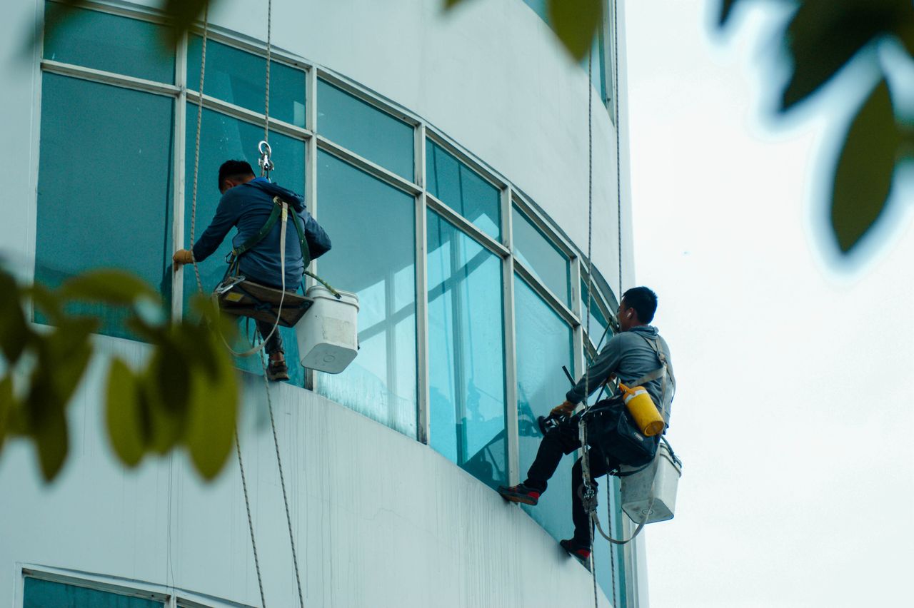 Window cleaners suspended on ropes clean a high-rise buildings glass exterior.